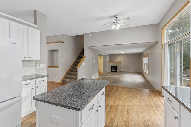 kitchen featuring a kitchen island, freestanding refrigerator, a tile fireplace, light wood-style floors, and backsplash