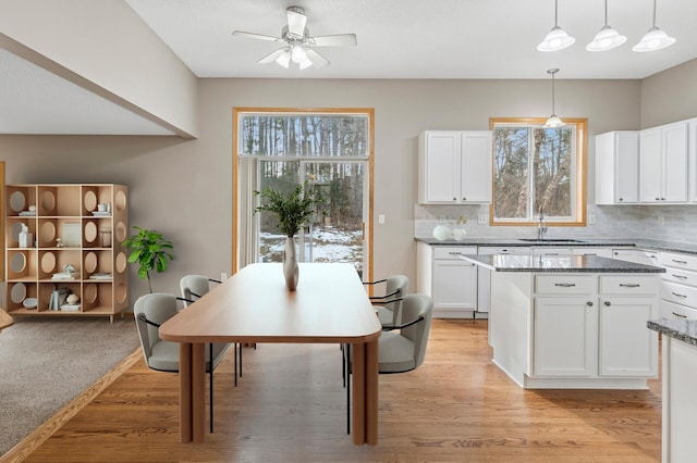 kitchen with a sink, light stone counters, backsplash, a kitchen island, and white cabinetry