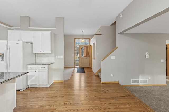 kitchen with light stone counters, visible vents, decorative backsplash, white cabinets, and white fridge with ice dispenser