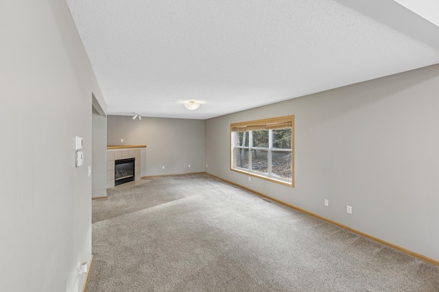 unfurnished living room featuring baseboards, a tile fireplace, a textured ceiling, and carpet