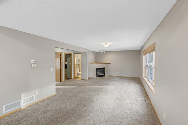 unfurnished living room with light carpet, visible vents, a fireplace, and baseboards