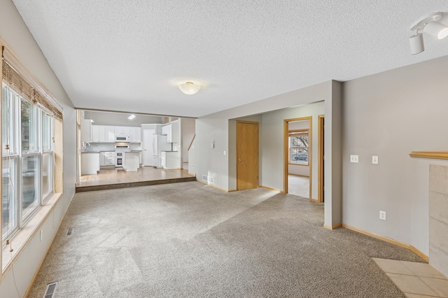 unfurnished living room with a sink, light carpet, and a textured ceiling