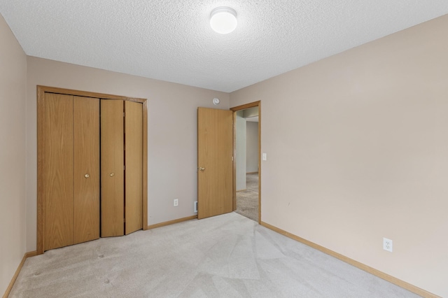 unfurnished bedroom with a closet, light carpet, a textured ceiling, and baseboards