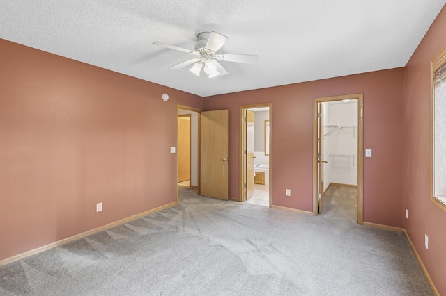 unfurnished bedroom with a walk in closet, baseboards, carpet, ensuite bathroom, and a textured ceiling