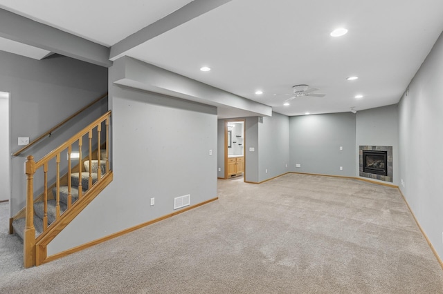 finished basement with visible vents, a tiled fireplace, stairs, carpet floors, and recessed lighting