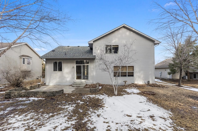 snow covered back of property featuring a shingled roof and entry steps