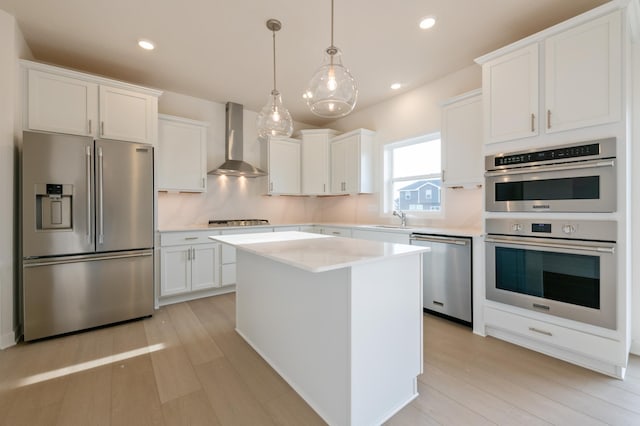 kitchen with wall chimney exhaust hood, appliances with stainless steel finishes, a center island, white cabinetry, and a sink