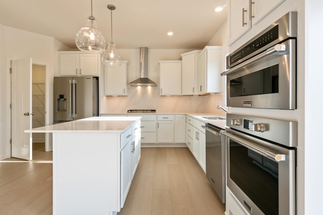 kitchen with appliances with stainless steel finishes, white cabinets, a kitchen island, and wall chimney range hood