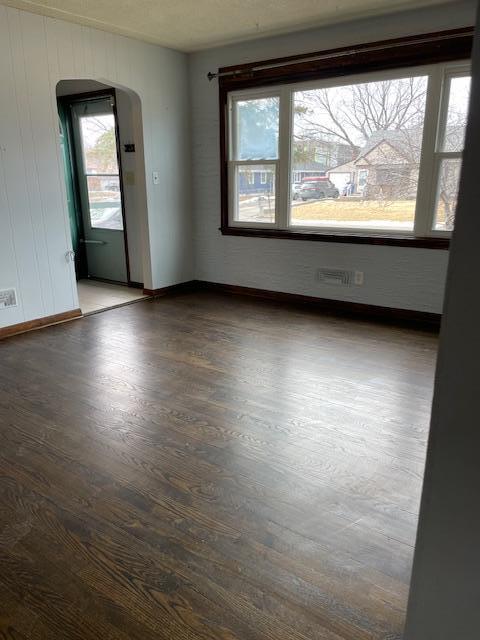 spare room with arched walkways, baseboards, and wood finished floors