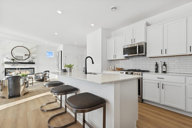 kitchen featuring a center island with sink, light wood-style flooring, appliances with stainless steel finishes, white cabinets, and a sink