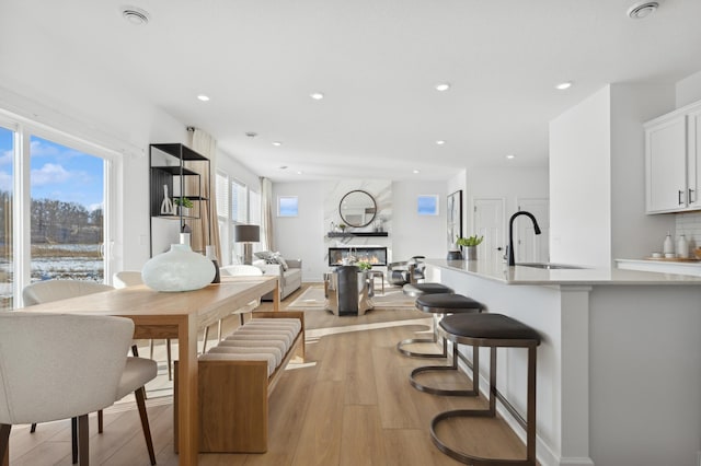 dining area with light wood-style floors, recessed lighting, and a premium fireplace