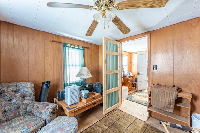 living area with a ceiling fan and wood walls