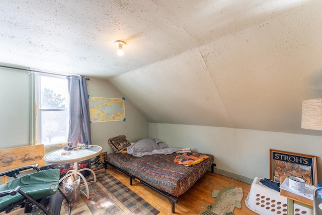 bedroom featuring lofted ceiling, a textured ceiling, baseboards, and wood finished floors