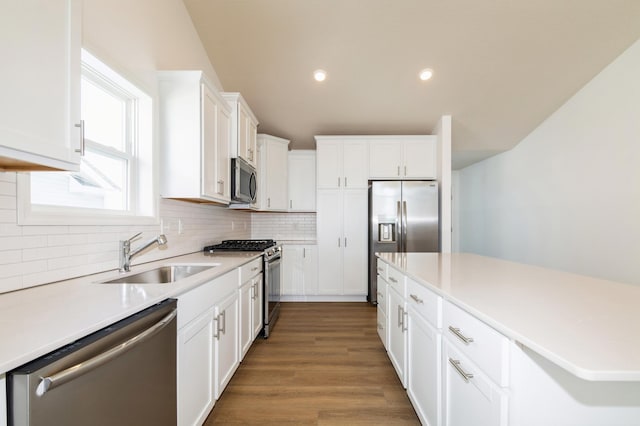 kitchen with a sink, backsplash, appliances with stainless steel finishes, white cabinets, and light countertops