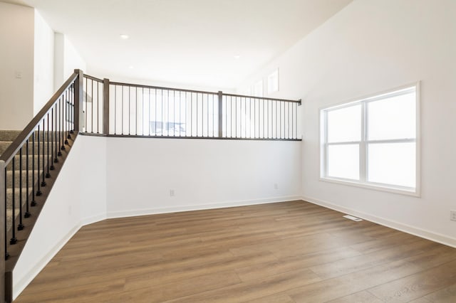 spare room featuring visible vents, a towering ceiling, baseboards, and wood finished floors