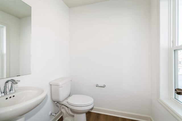 half bathroom with wood finished floors, toilet, baseboards, and a sink