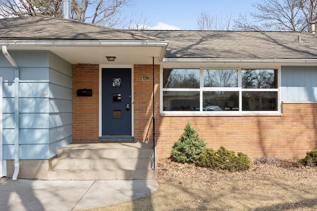 entrance to property featuring brick siding and a shingled roof