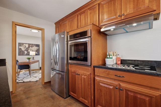 kitchen with under cabinet range hood, dark stone countertops, appliances with stainless steel finishes, and brown cabinetry