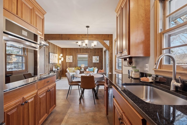 kitchen featuring wooden walls, open floor plan, stainless steel oven, an inviting chandelier, and a sink