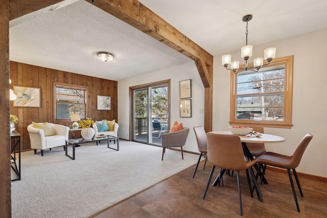 dining room with beamed ceiling, a notable chandelier, wooden walls, carpet flooring, and baseboards