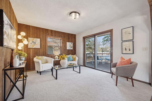 carpeted living area with wood walls, a textured ceiling, and baseboards