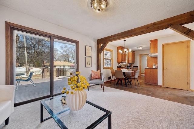 living area with light carpet, beamed ceiling, a textured ceiling, and an inviting chandelier