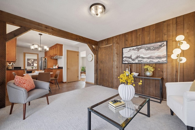 living area with wooden walls, a notable chandelier, beamed ceiling, and light carpet