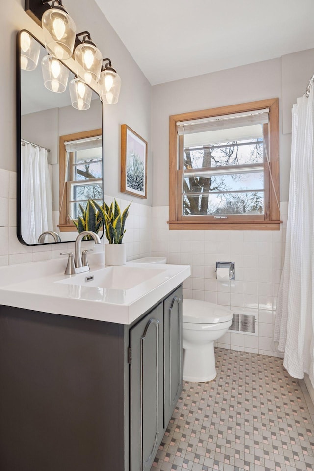 full bath with visible vents, toilet, vanity, wainscoting, and tile walls