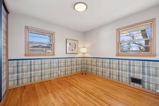 unfurnished room featuring a wealth of natural light, a wainscoted wall, visible vents, and wood finished floors