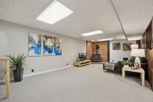 carpeted living area featuring a drop ceiling, a wood stove, and baseboards