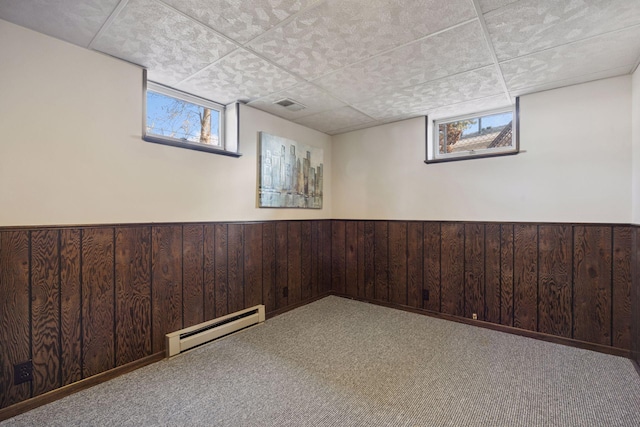 basement with visible vents, a wainscoted wall, wood walls, carpet flooring, and a baseboard radiator