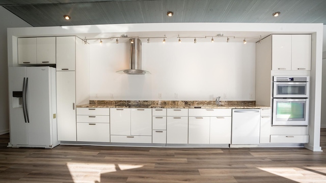 kitchen featuring white appliances, dark stone counters, wood finished floors, wall chimney range hood, and white cabinetry