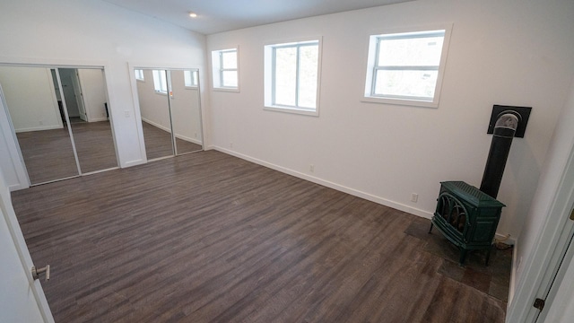 unfurnished bedroom featuring dark wood-style flooring, two closets, a wood stove, vaulted ceiling, and baseboards