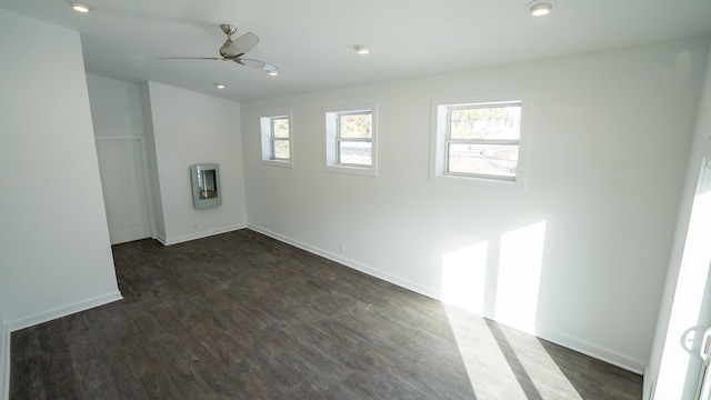 unfurnished room featuring a ceiling fan, baseboards, dark wood finished floors, and a wealth of natural light