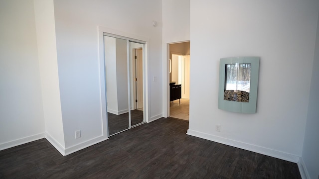 unfurnished bedroom with a towering ceiling, a closet, baseboards, and dark wood-style flooring