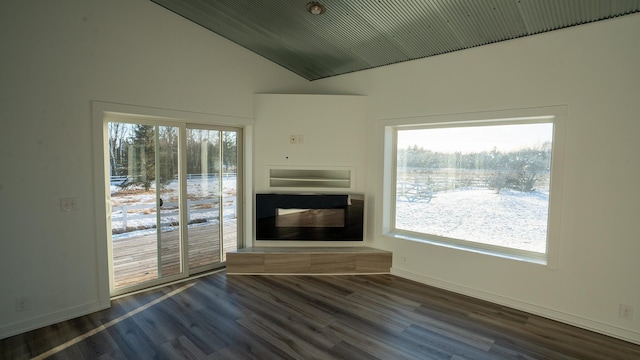 unfurnished living room with dark wood-style floors, baseboards, vaulted ceiling, and a fireplace with raised hearth