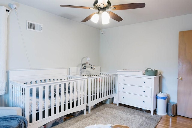 bedroom featuring a crib, visible vents, and a ceiling fan