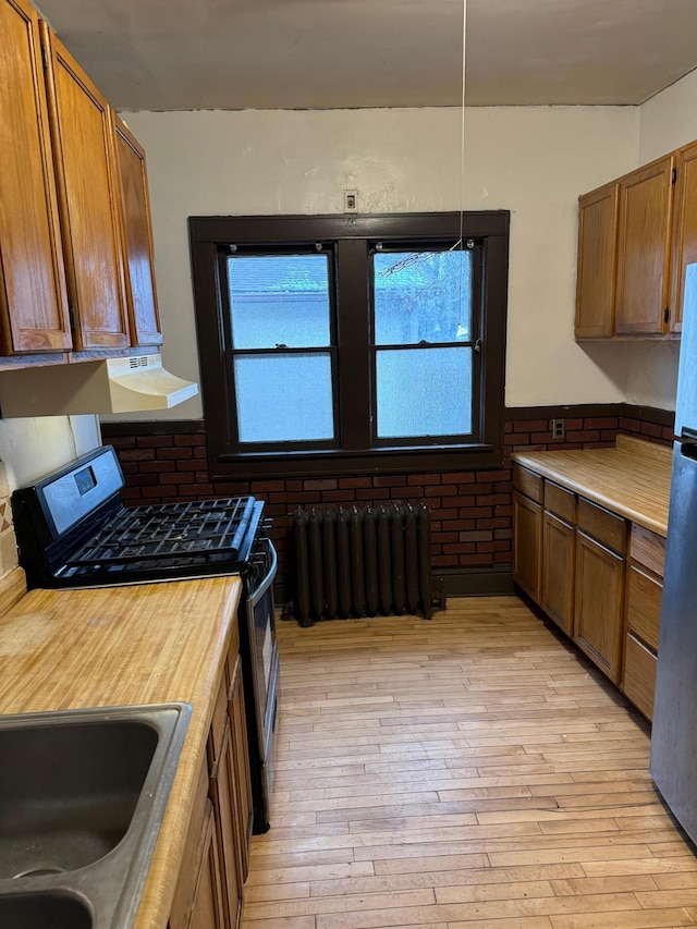 kitchen with light countertops, light wood-style flooring, radiator heating unit, gas stove, and freestanding refrigerator