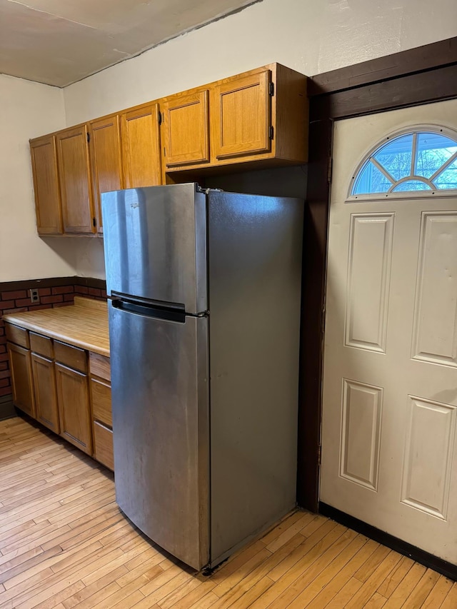 kitchen featuring light wood-style flooring, brown cabinets, light countertops, and freestanding refrigerator