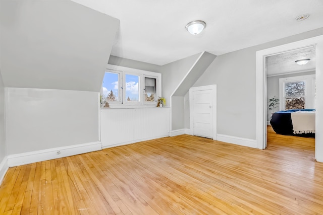 bonus room with a healthy amount of sunlight, light wood-style floors, baseboards, and vaulted ceiling