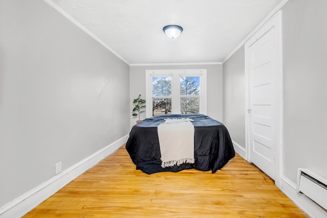 bedroom featuring a baseboard heating unit, ornamental molding, wood finished floors, and baseboards