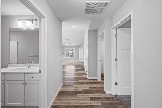 hallway with dark wood finished floors, baseboards, visible vents, and a sink