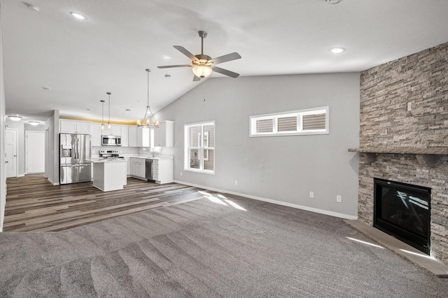 unfurnished living room featuring ceiling fan with notable chandelier, a fireplace, baseboards, and dark carpet