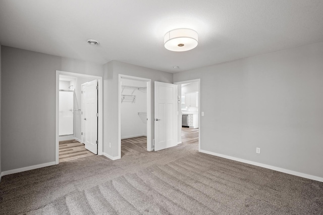 unfurnished bedroom with baseboards, ensuite bath, a spacious closet, a closet, and carpet flooring