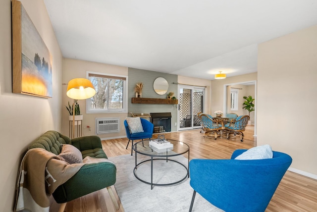 living area featuring a brick fireplace, a wall unit AC, baseboards, and wood finished floors