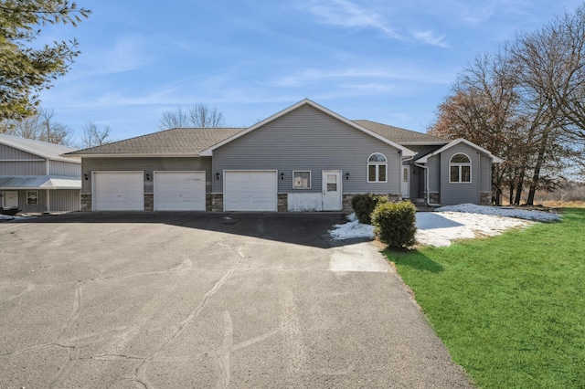 single story home with stone siding, aphalt driveway, roof with shingles, an attached garage, and a front yard