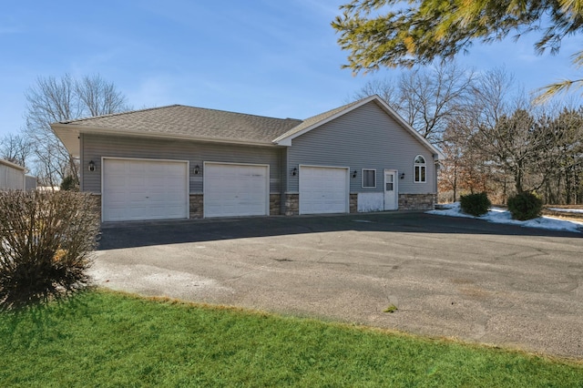 view of home's exterior featuring driveway, stone siding, a garage, and roof with shingles