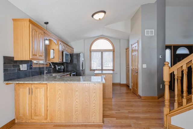 kitchen featuring lofted ceiling, visible vents, appliances with stainless steel finishes, a sink, and a peninsula