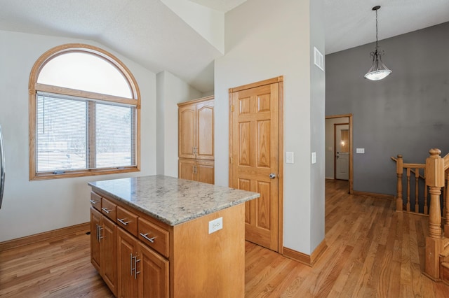 kitchen with light wood finished floors, a kitchen island, light stone counters, and decorative light fixtures