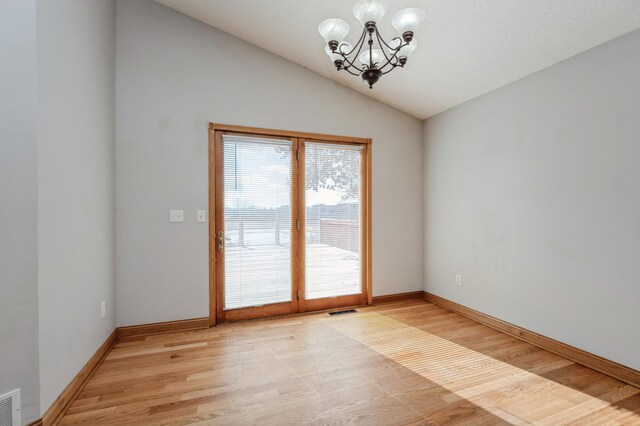 empty room featuring visible vents, light wood-style floors, vaulted ceiling, baseboards, and an inviting chandelier